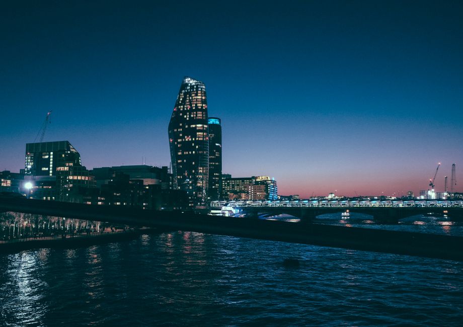 An aerial view of the London cityscape showcasing the River Thames flowing through the urban area, with several bridges crossing the river and a mixture of modern and historic buildings along the shor