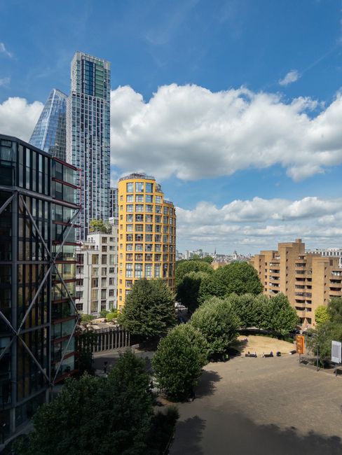 A view of the London skyline across the River Thames during daytime, featuring modern skyscrapers such as The Scalpel and The Walkie-Talkie building, with a historic railway bridge in the foreground.